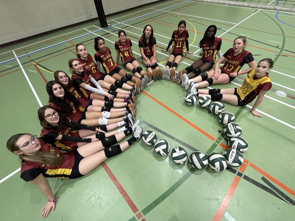 Des filles assises au sol forment un coeur avec leur peid et des ballons de volleyball